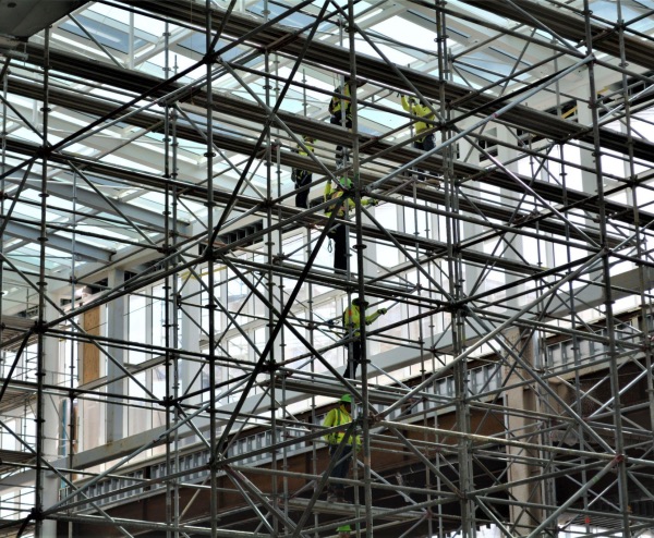 Construction workers in safety vests on scaffolding inside a glass-roofed building